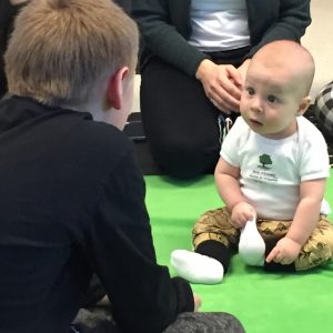 Baby looks up at a boy in the foreground, whose back is turned to the camera