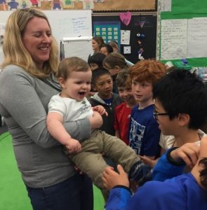 A mother holds her baby up so students can sing to him.