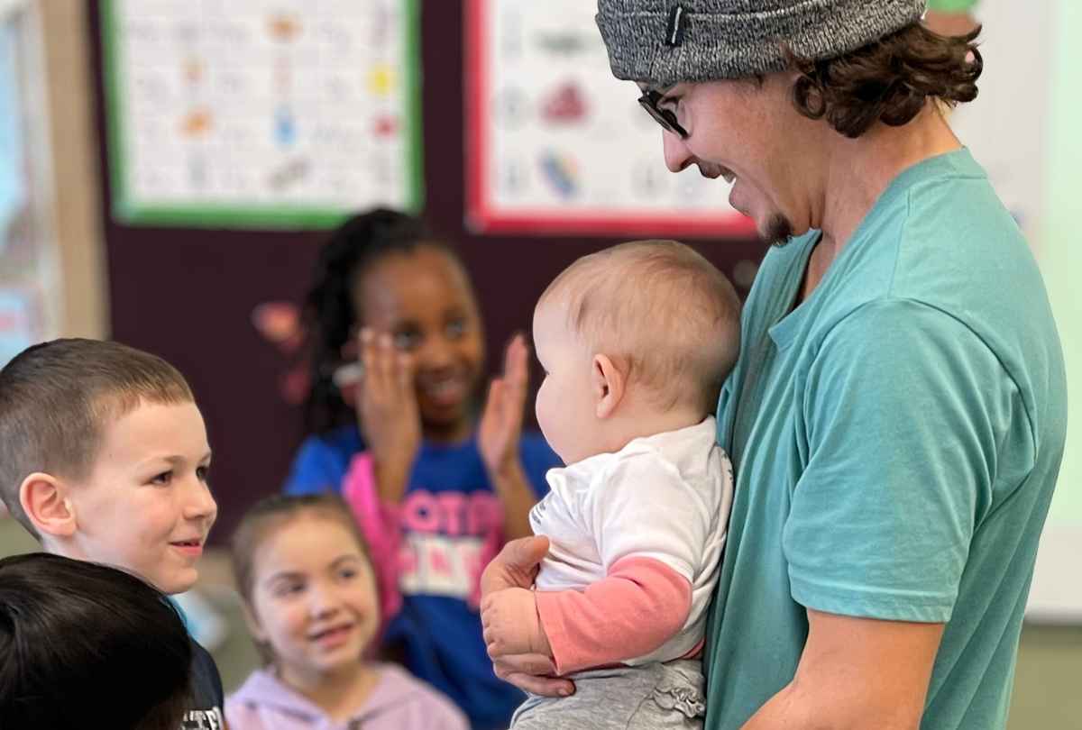 Father holds baby and shows the baby to delighted boy